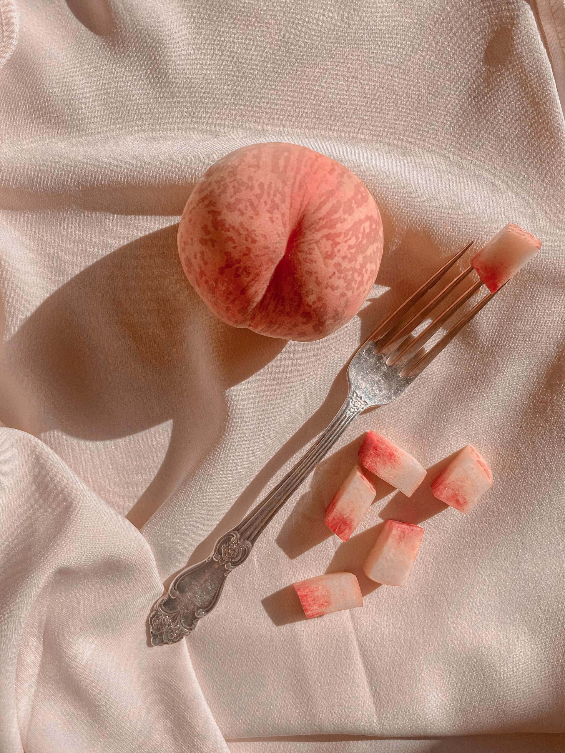 Elegant composition of a ripe peach with slices and shadow on soft fabric, capturing a vintage feel.